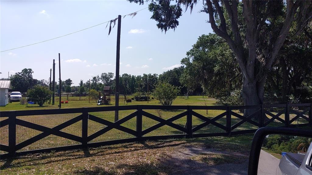 A black wooden fence borders a grassy yard with a playground and large trees — 3008 N MARYLAND AVENUE, PLANT CITY, FL