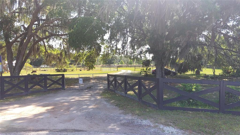 A gravel driveway leads through a metal gate flanked by dark wooden cross-buck fencing — 3008 N MARYLAND AVENUE, PLANT CITY, FL