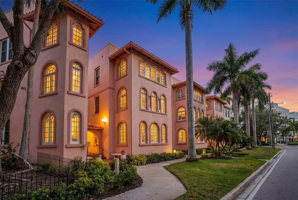 A multi-story pink stucco building with arched windows and palm trees at dusk — 1221 N PALM AVENUE UNIT 106/107, SARASOTA, FL