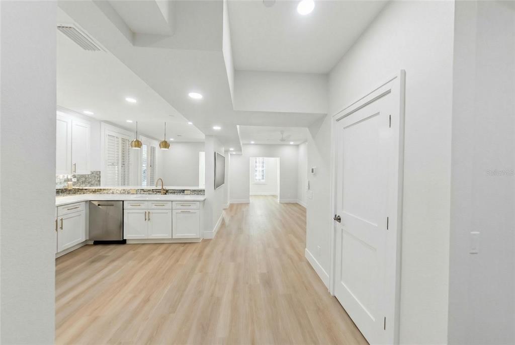 A white kitchen with light wood flooring opens into a hallway leading to another room — 1221 N PALM AVENUE UNIT 106/107, SARASOTA, FL