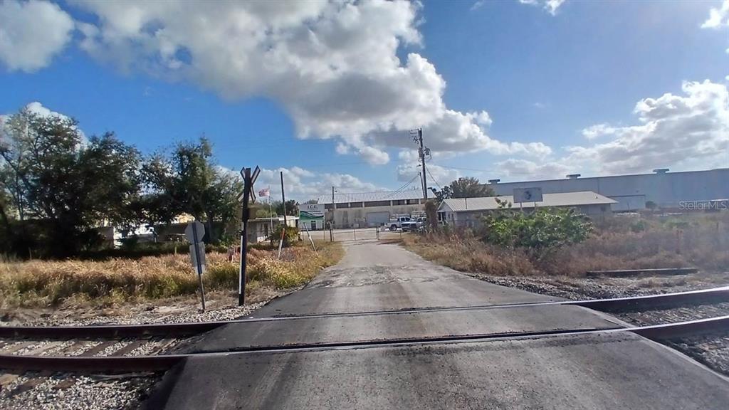A paved road crosses railroad tracks leading toward a fenced industrial building under a cloudy sky — 2295 US HIGHWAY 92 E, PLANT CITY, FL