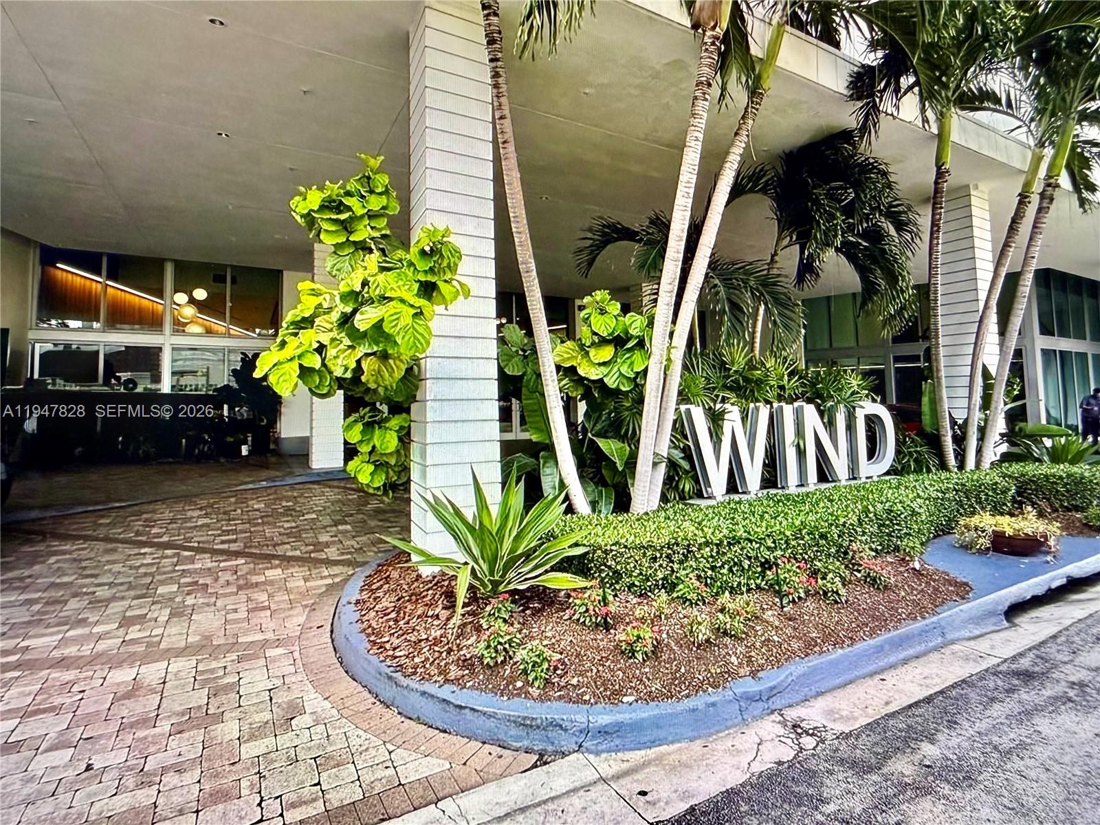 The exterior entrance of a building features a large sign reading WIND and landscaping — 350 S Miami Ave # 2912, Miami FL 33130, MIAMI, FL