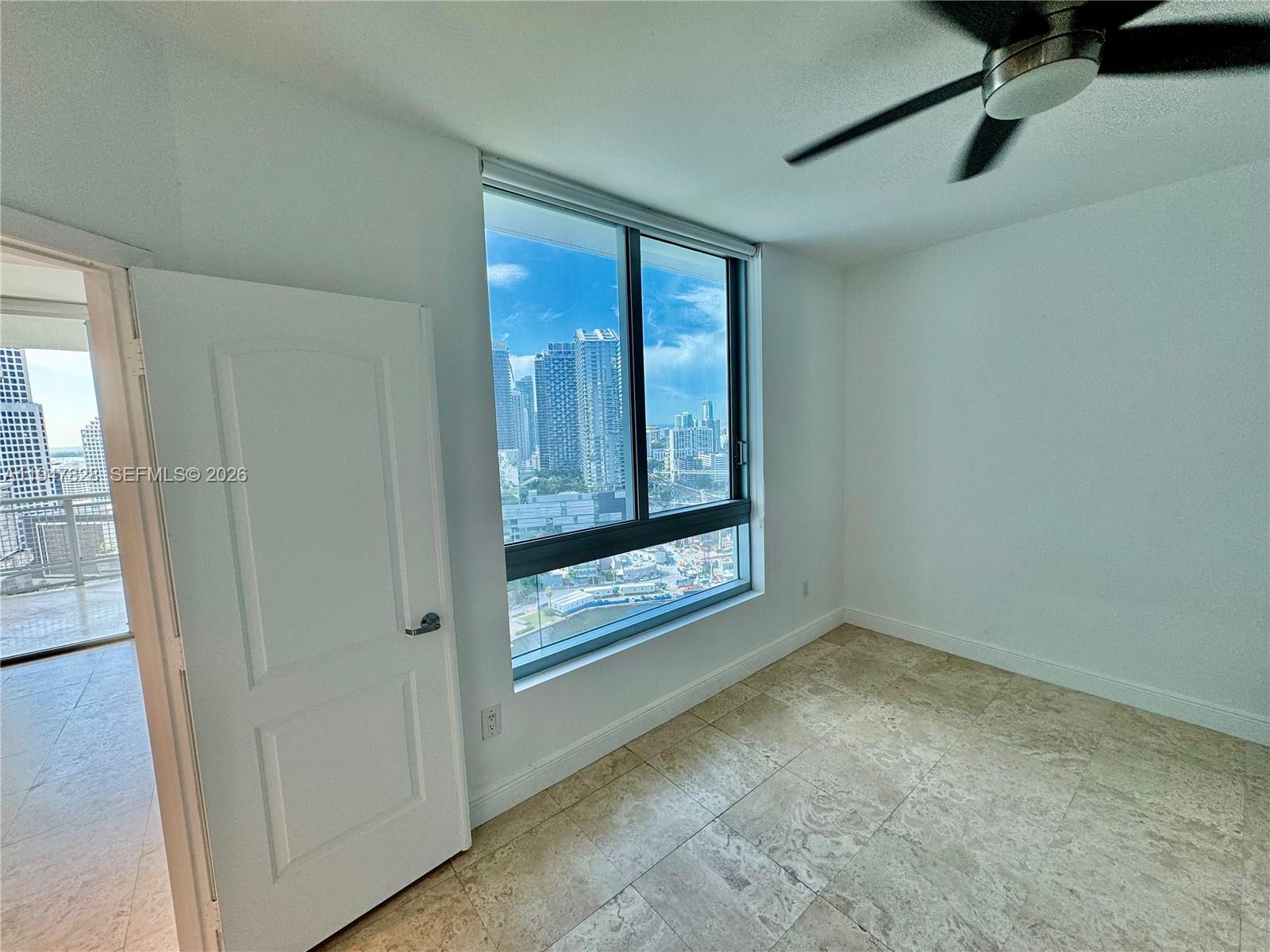 An empty room features tile flooring, a ceiling fan, and a large window overlooking city buildings — 350 S Miami Ave # 2912, Miami FL 33130, MIAMI, FL