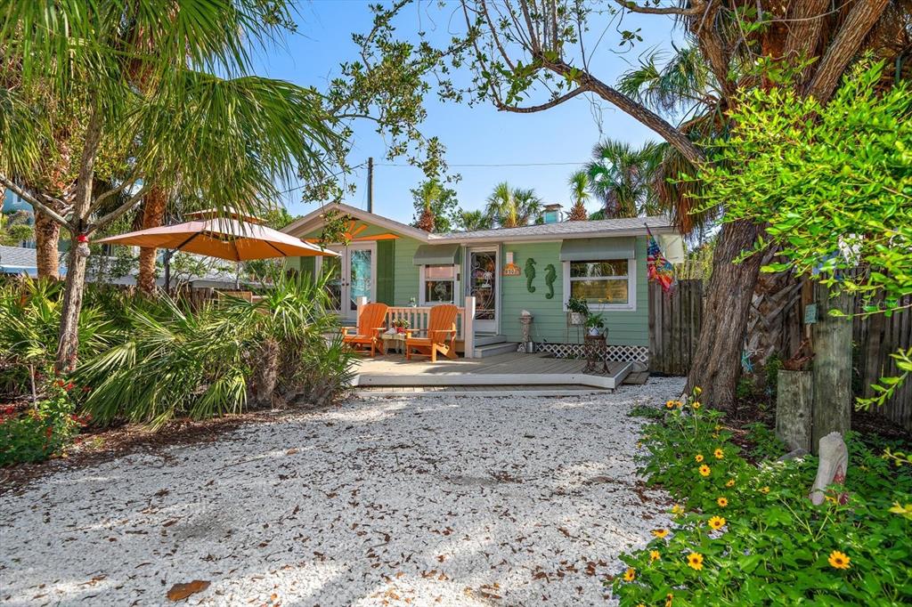 A light green cottage with a wooden deck, orange chairs, and a gravel driveway — 8403 W GULF BOULEVARD, TREASURE ISLAND, FL