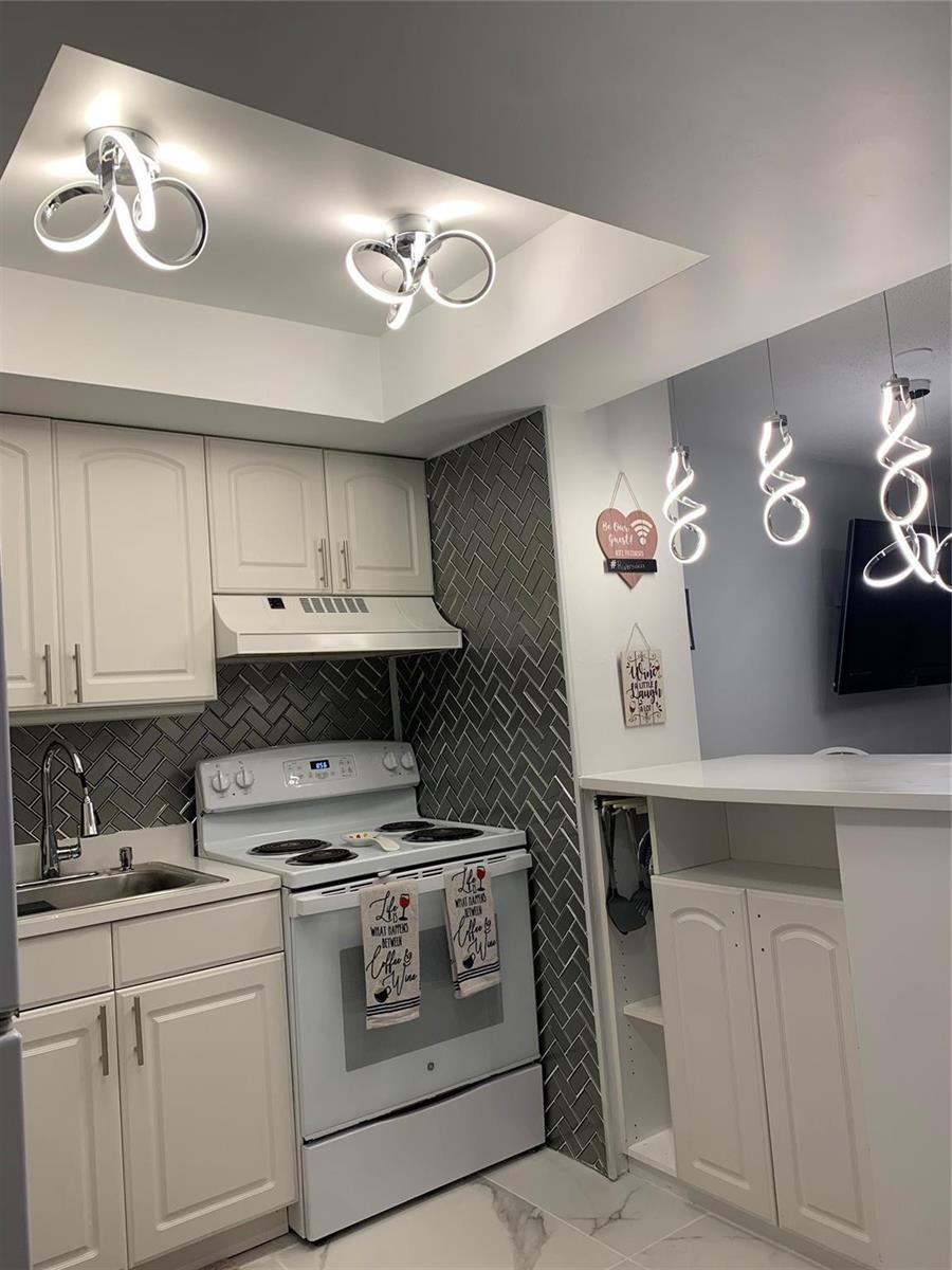 A kitchen features white cabinets, a grey herringbone backsplash, and modern spiral light fixtures — 1110 N Riverside Drive # 25, Pompano Beach FL 33062, POMPANO BEACH, FL