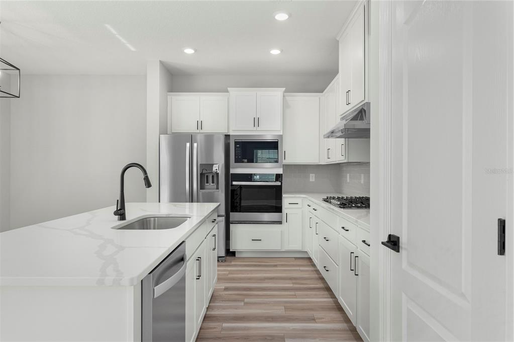 A modern kitchen features white cabinetry, stainless steel appliances, and a central island with seating — 7833 MARLOW PLACE, KISSIMMEE, FL