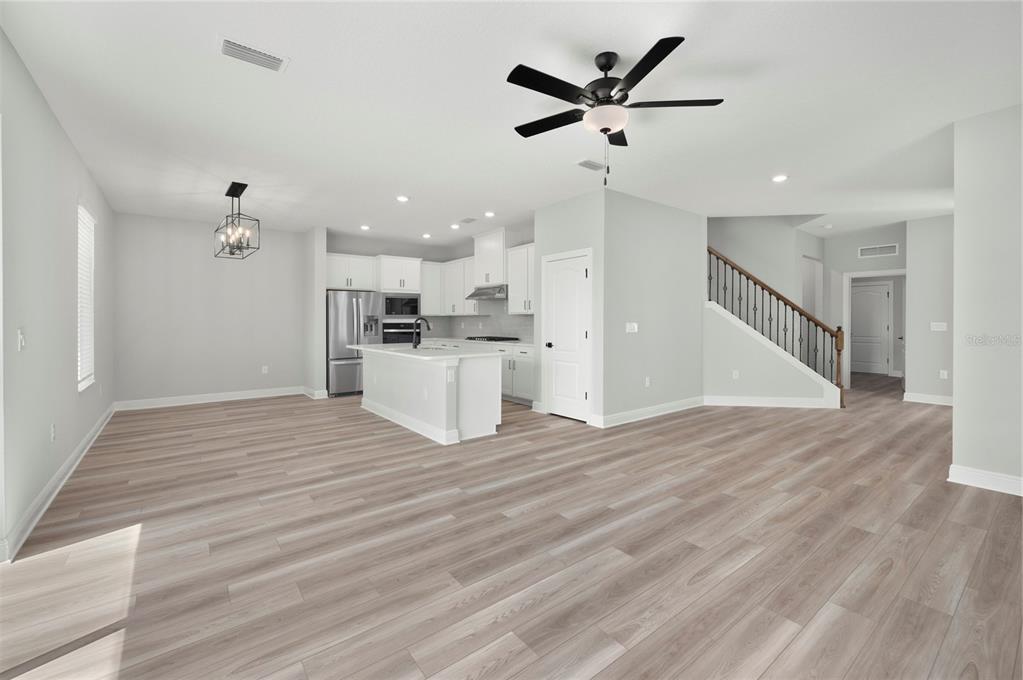 An open-concept kitchen and living area feature white cabinetry, a center island, and wood-look flooring — 7833 MARLOW PLACE, KISSIMMEE, FL
