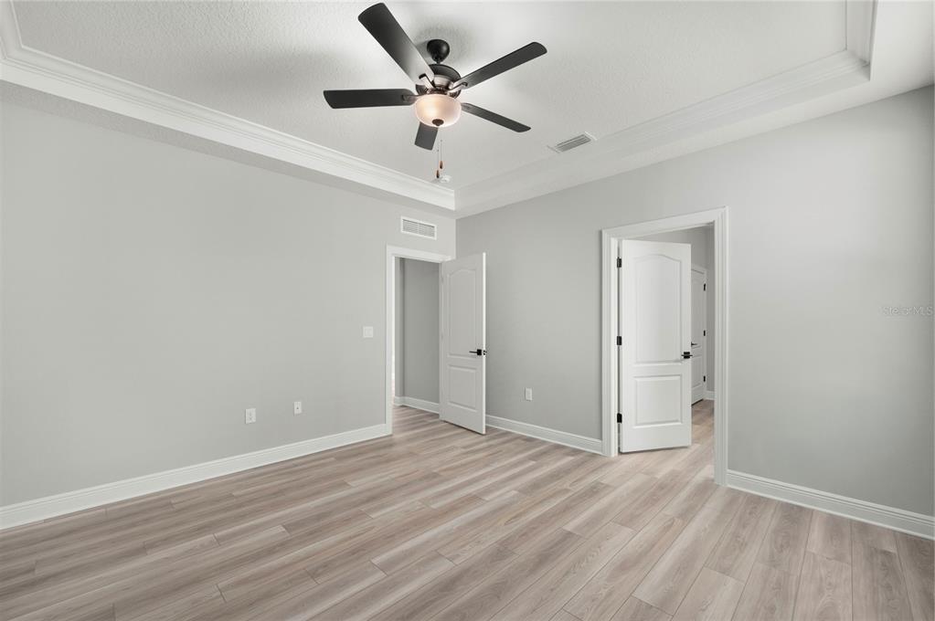 An empty room with light gray walls, wood-look flooring, a ceiling fan, and two doorways — 7833 MARLOW PLACE, KISSIMMEE, FL