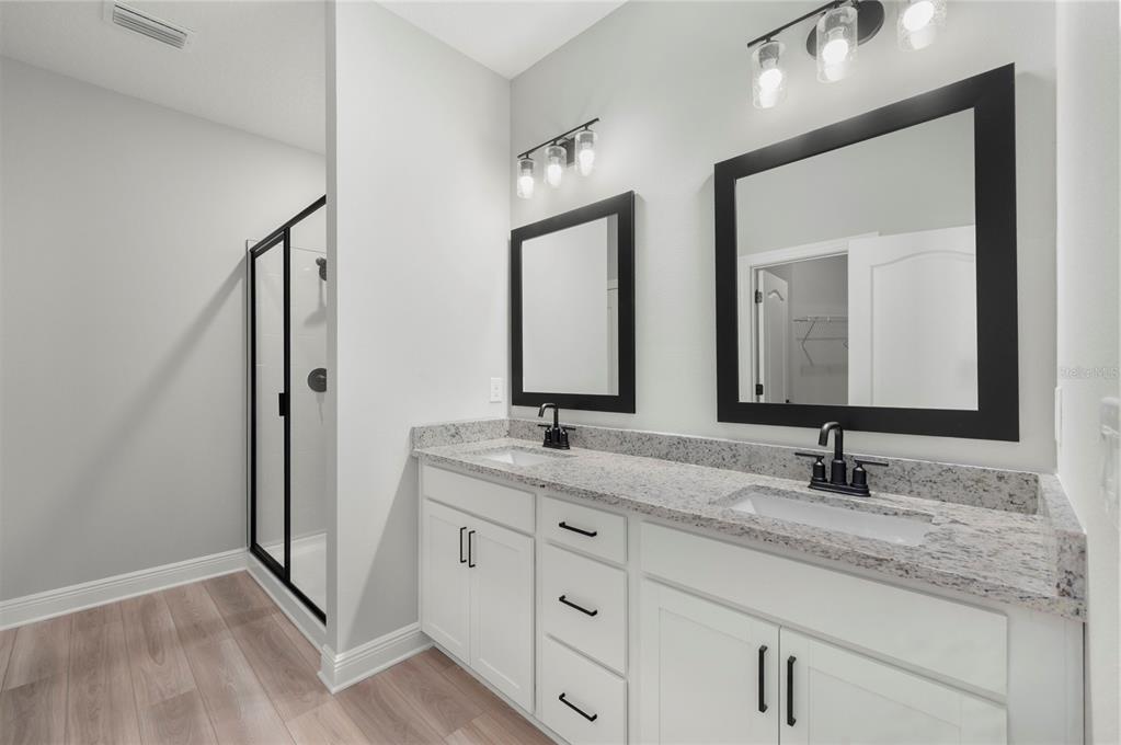 A bathroom features a double vanity with white cabinets, granite countertops, and black-framed mirrors — 7833 MARLOW PLACE, KISSIMMEE, FL