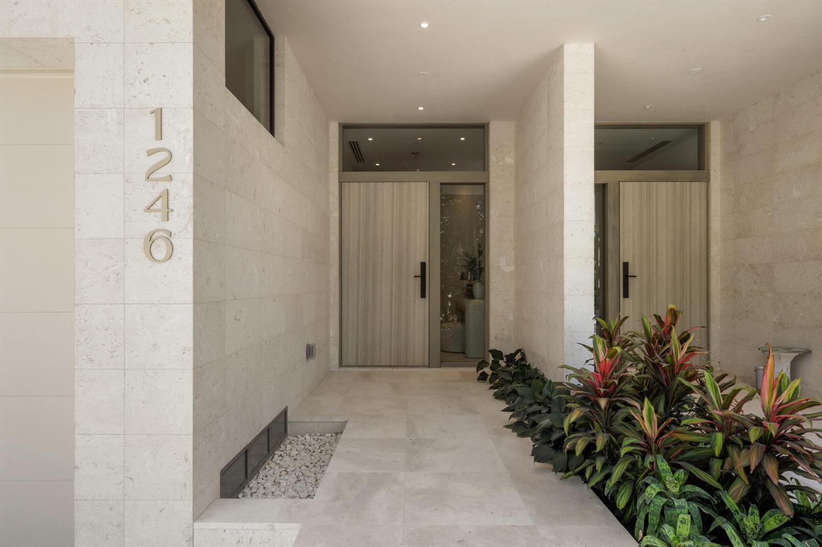 A modern entryway features two wood-grain doors, light stone walls, and a small garden bed — 1258 George Bush Boulevard, Delray Beach FL 33483, DELRAY BEACH, FL