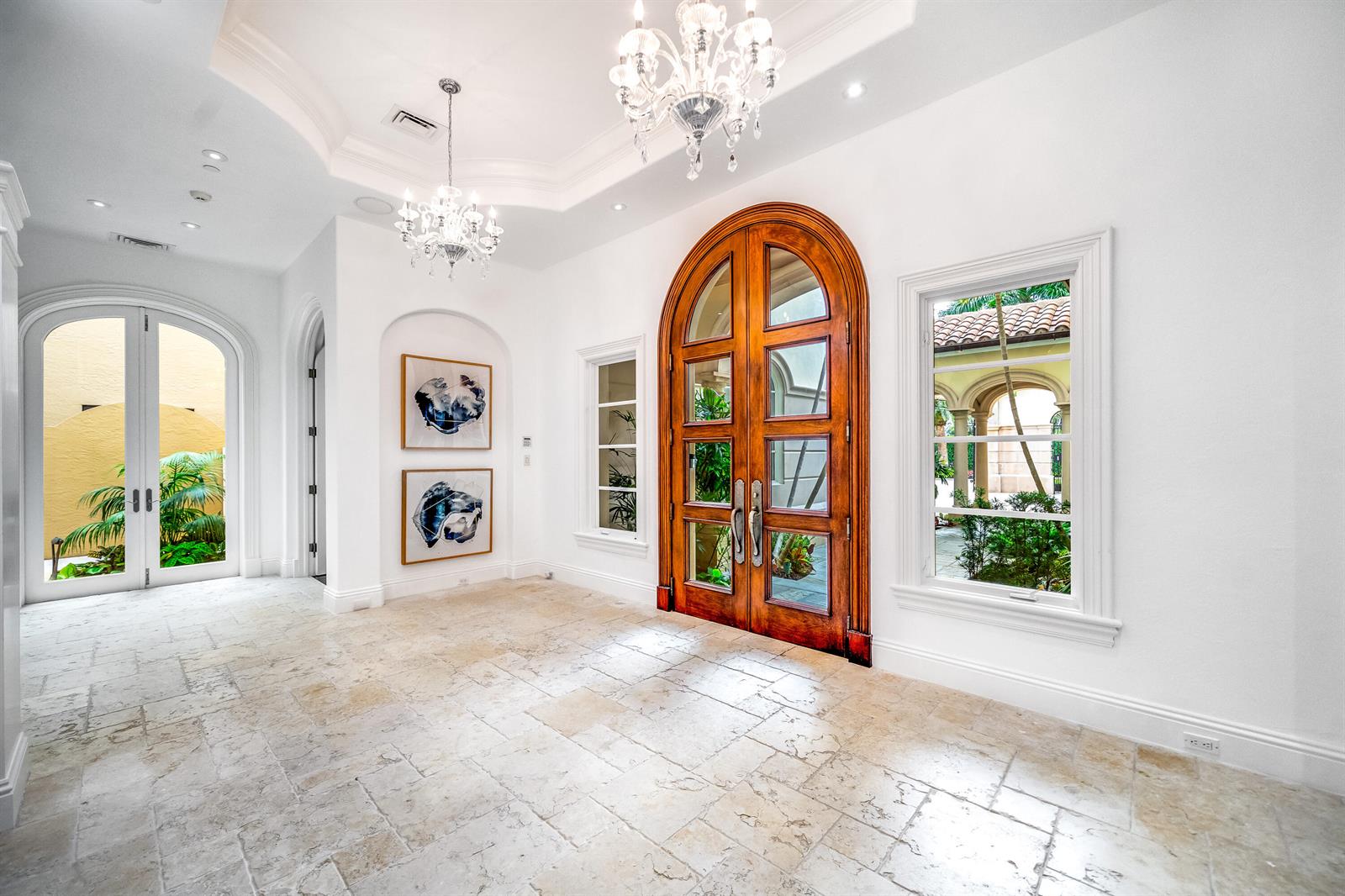 A bright foyer features stone flooring, two crystal chandeliers, and a large arched wooden door — 361 Mizner Lake Estates Drive, Boca Raton FL 33432, BOCA RATON, FL