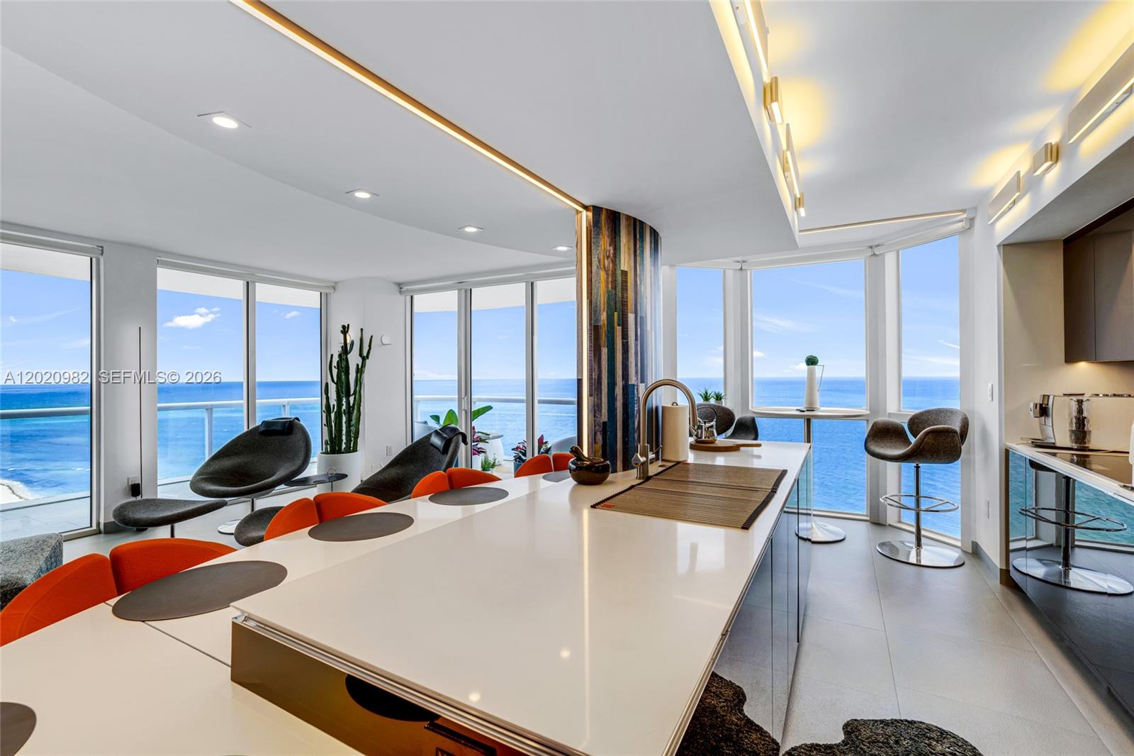 A modern kitchen and dining area features a white island, orange chairs, and ocean views — 6365 Collins Ave # 2301, Miami Beach FL 33141, MIAMI BEACH, FL