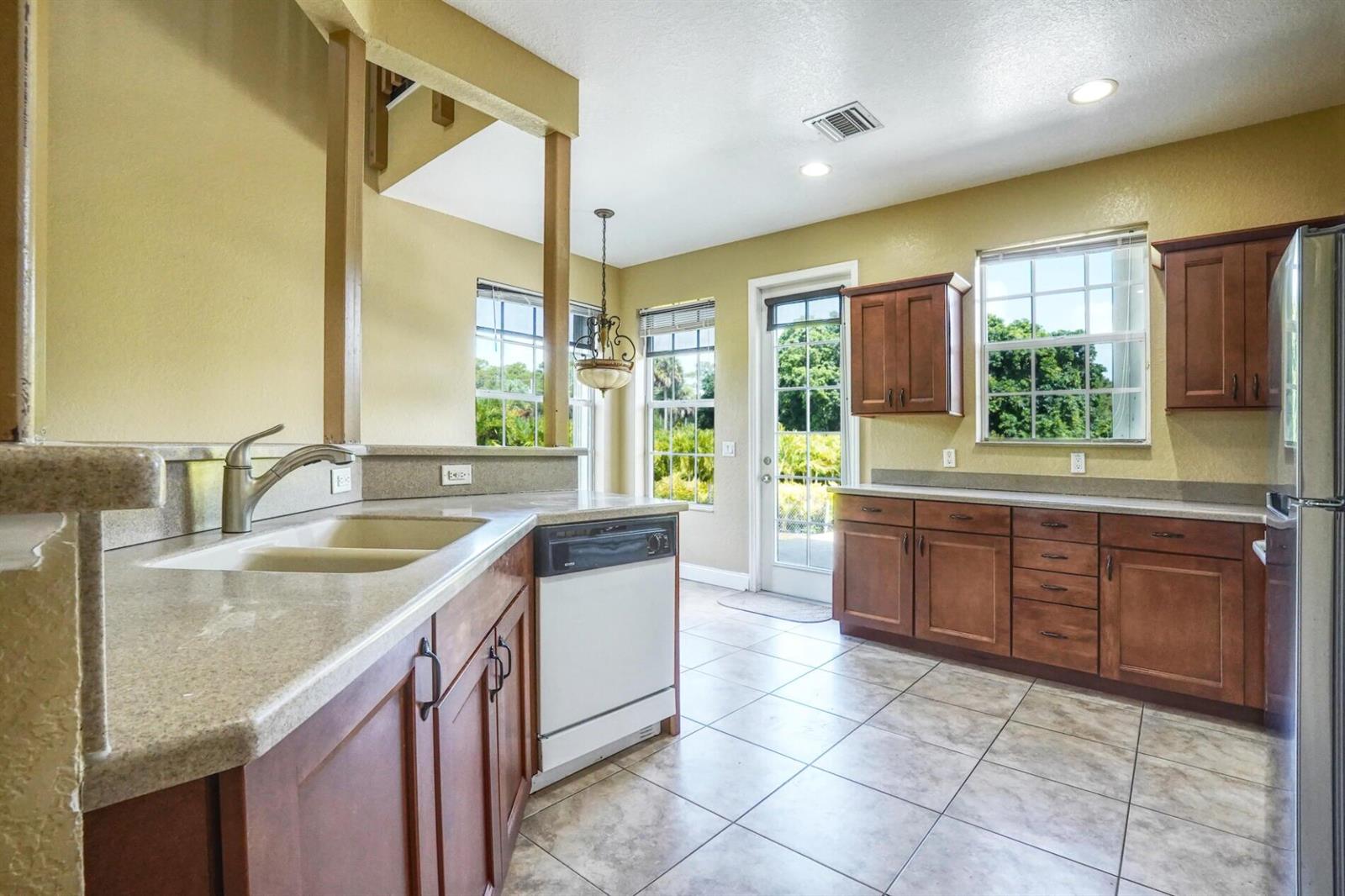 A kitchen with wood cabinets, stone countertops, tile floors, and a glass door to outside — 1550 C Road, FL 33470, FL