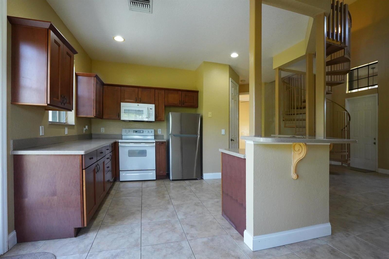 A kitchen with wood cabinets, stainless steel appliances, tile floors, and a spiral staircase nearby — 1550 C Road, FL 33470, FL