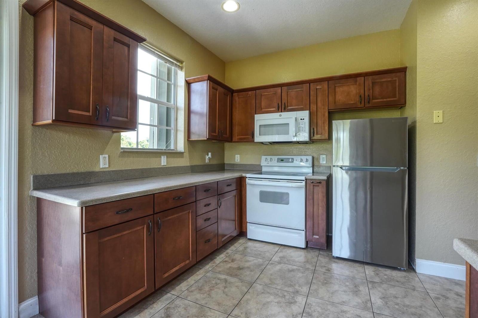 A kitchen with wood cabinets, stainless steel refrigerator, white appliances, and tan tile flooring — 1550 C Road, FL 33470, FL