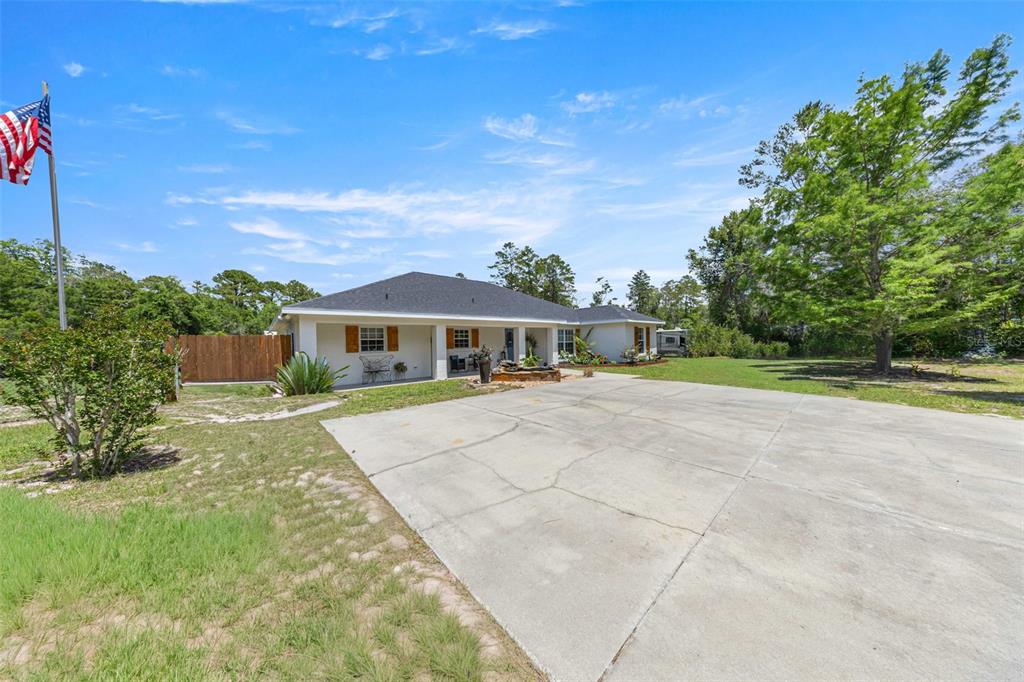 A single-story house with a large concrete driveway, a flag pole, and surrounding trees — 495 FISHER ROAD, OCKLAWAHA, FL