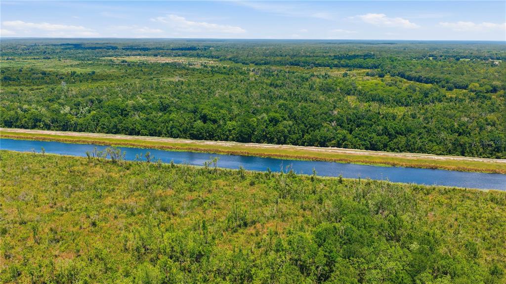 An aerial view shows a narrow canal running through a vast, forested landscape — 495 FISHER ROAD, OCKLAWAHA, FL