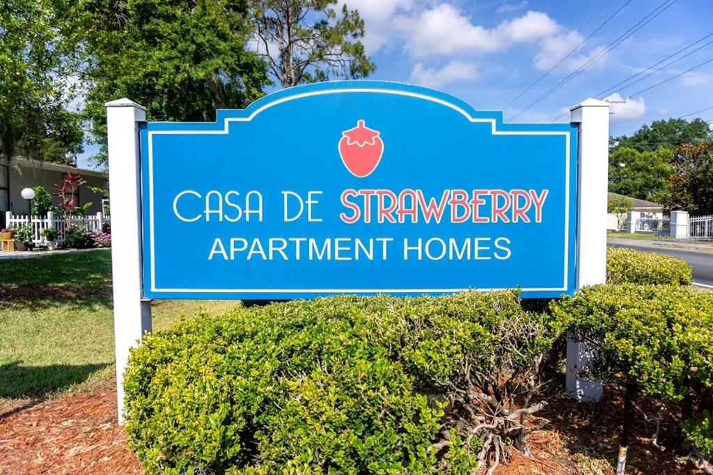 A blue sign for Casa De Strawberry Apartment Homes stands in front of green bushes — 1400 STRAWBERRY PLACE UNIT 33, PLANT CITY, FL