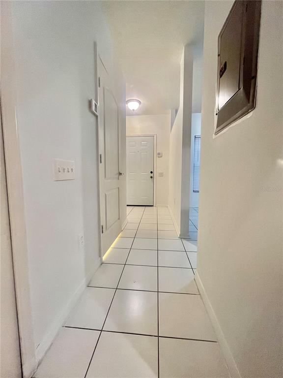 A hallway with white tile flooring leads to a white front door — 1211 KENNEWICK COURT, WESLEY CHAPEL, FL