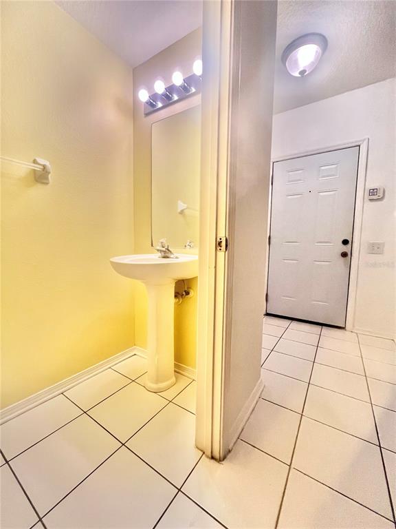 A small bathroom with a pedestal sink and tile flooring sits next to an entryway — 1211 KENNEWICK COURT, WESLEY CHAPEL, FL