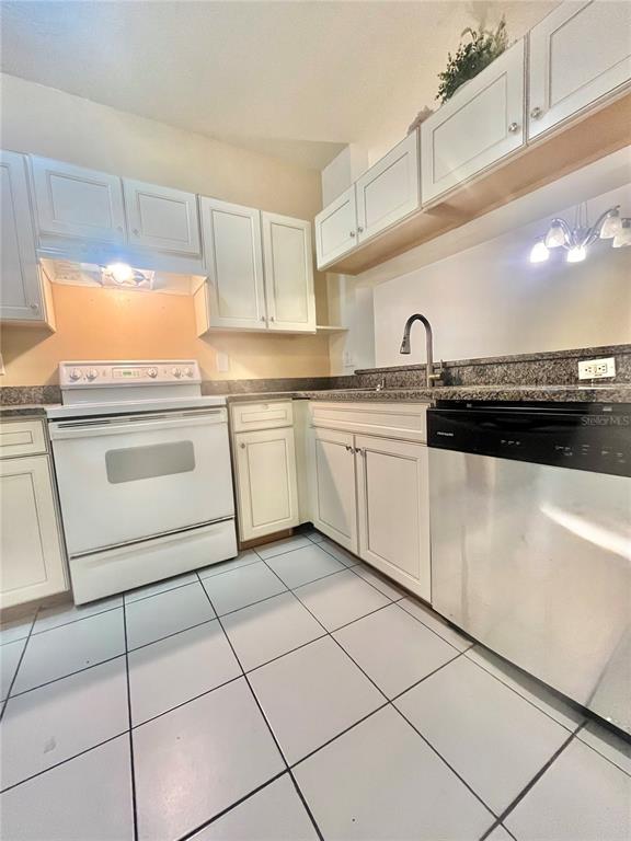 A kitchen features white cabinets, a white stove, a stainless steel dishwasher, and tiled floors — 1211 KENNEWICK COURT, WESLEY CHAPEL, FL