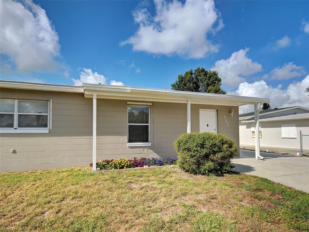 A single-story house with tan block siding, a covered entryway, and a small front garden — 8215 AGRESS AVENUE, NORTH PORT, FL