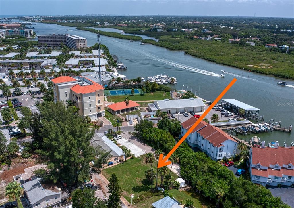 An aerial view shows a vacant lot near a waterway, boat docks, and residential buildings — WHISPERING PINES DRIVE, INDIAN SHORES, FL