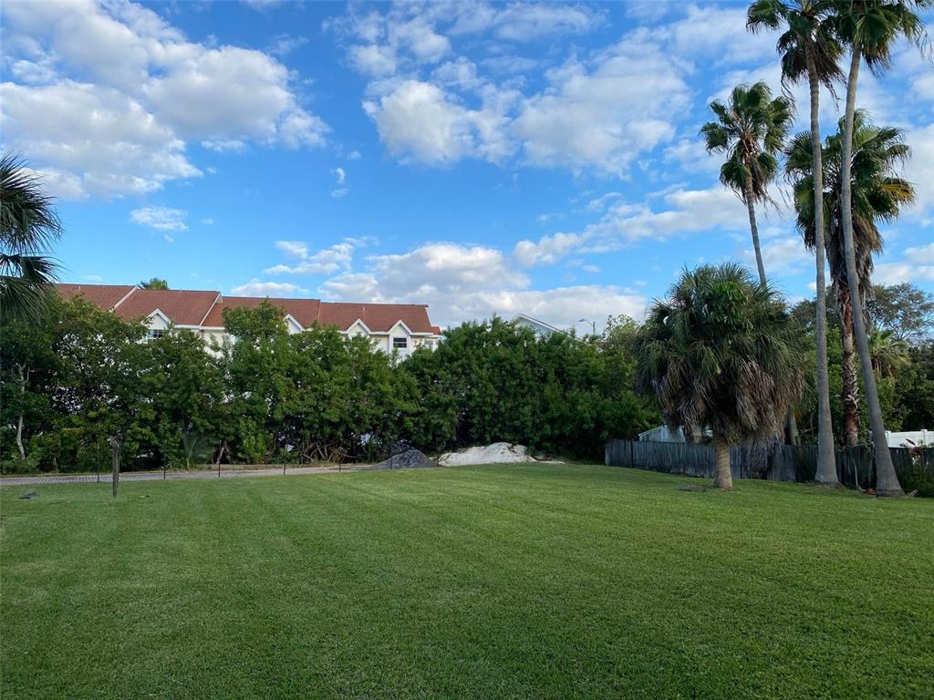 A grassy lot features palm trees, dense foliage, and a residential building in the background — WHISPERING PINES DRIVE, INDIAN SHORES, FL