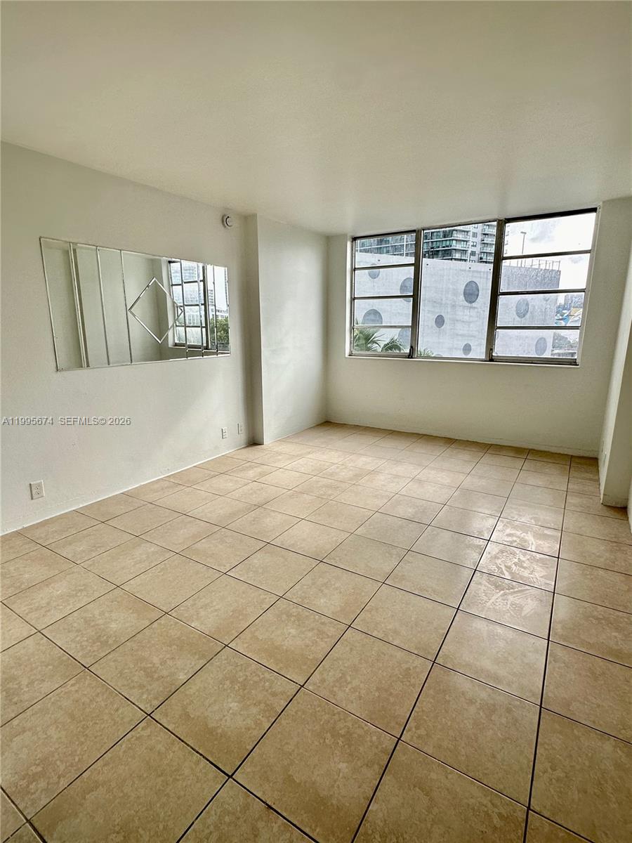 An empty room features light-colored tile flooring, white walls, a wall mirror, and large windows — 3301 NE 5th Ave # 618, Miami FL 33137, MIAMI, FL