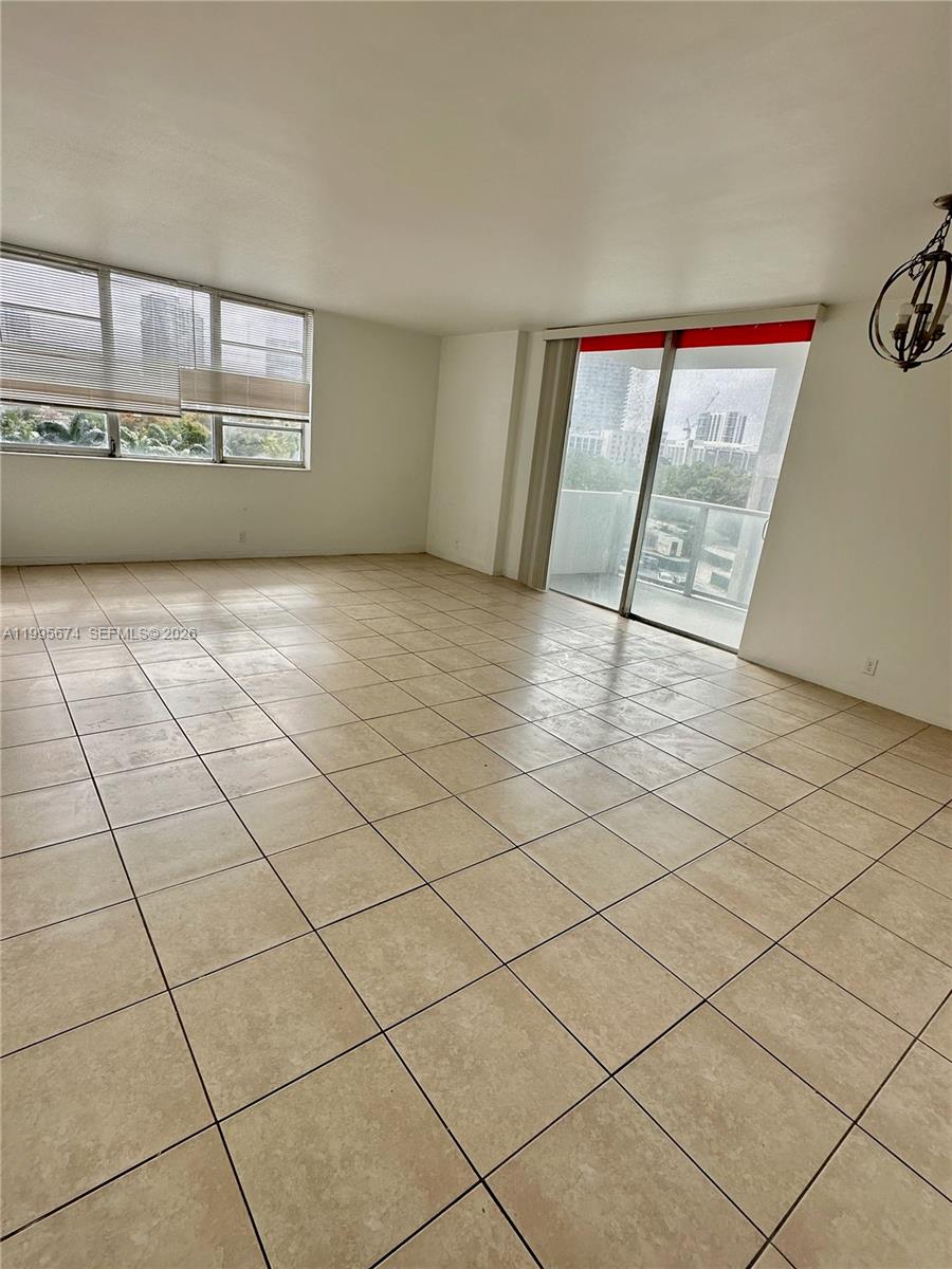 An empty room features beige tile flooring, a large window, and a sliding glass door — 3301 NE 5th Ave # 618, Miami FL 33137, MIAMI, FL