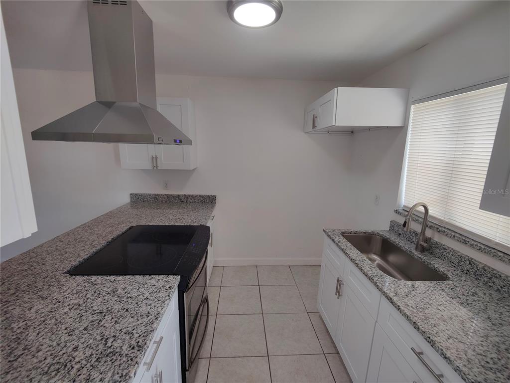 A kitchen features white cabinets, granite countertops, a stainless steel range hood, and tile flooring — 5835 CURRY FORD ROAD, ORLANDO, FL