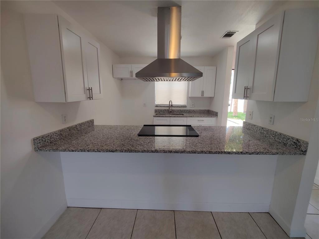 A kitchen features white cabinets, granite countertops, a central island cooktop, and a stainless hood — 5835 CURRY FORD ROAD, ORLANDO, FL