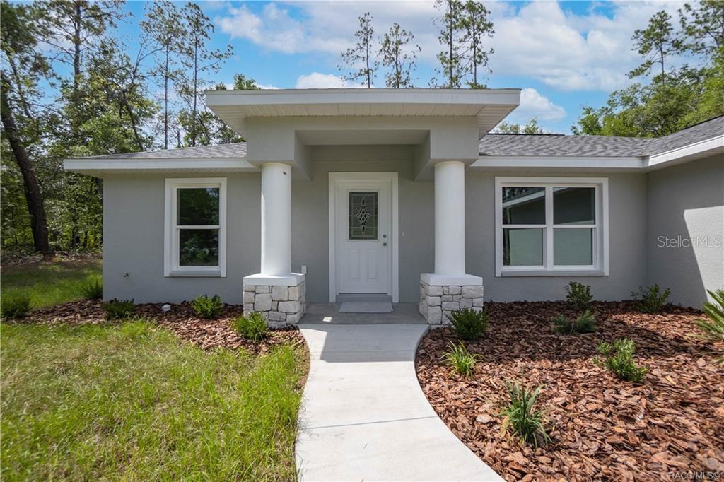 A gray house exterior features a front entrance with two white columns and stone bases — 8880 N CIRCULAR WAY, CITRUS SPRINGS, FL