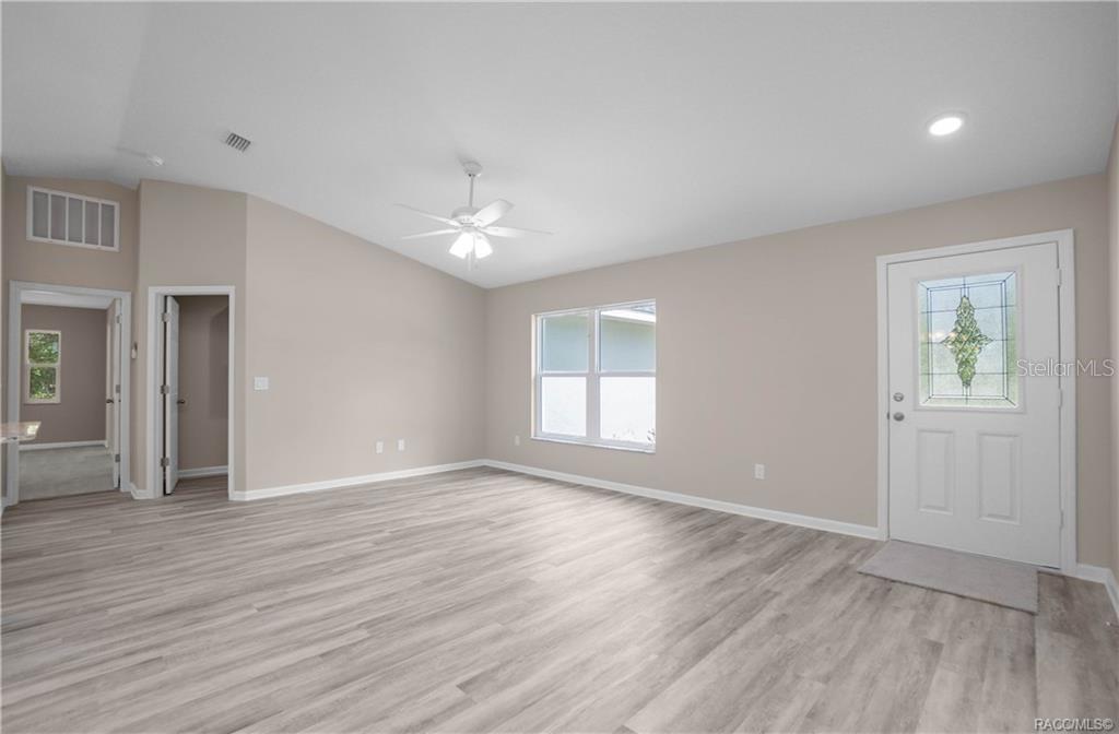 A living room with light wood-look flooring, beige walls, a ceiling fan, and an entry door — 8880 N CIRCULAR WAY, CITRUS SPRINGS, FL