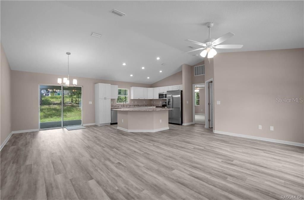 An open-concept kitchen and living area features white cabinets, stainless appliances, and light wood flooring — 8880 N CIRCULAR WAY, CITRUS SPRINGS, FL