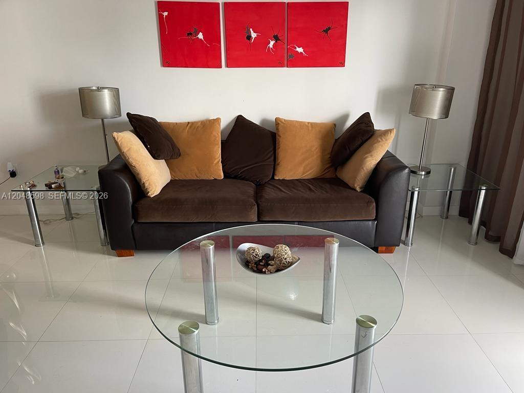A living room features a brown sofa with decorative pillows, glass tables, and red wall art — 5701 Collins Ave # 1411, Miami Beach FL 33140, MIAMI BEACH, FL