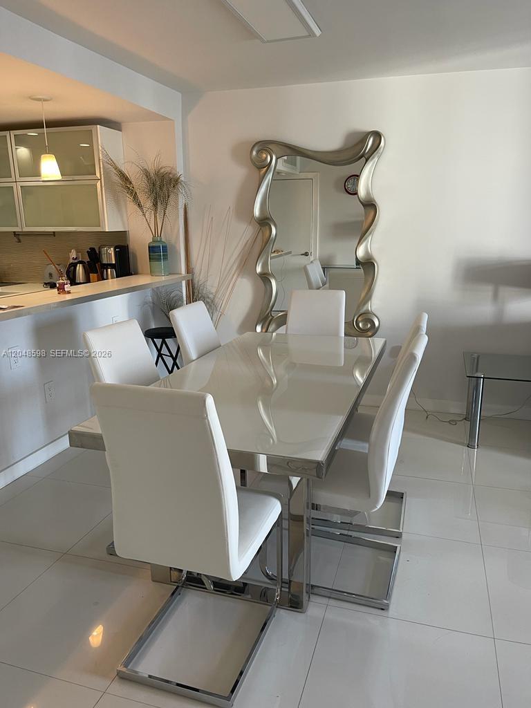 A dining room features a white table, six white chairs, and a large wavy mirror — 5701 Collins Ave # 1411, Miami Beach FL 33140, MIAMI BEACH, FL