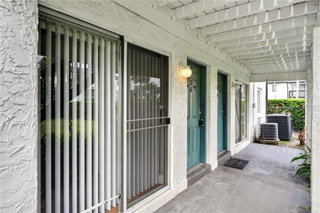 A covered outdoor walkway features two teal doors, sliding glass doors, and a concrete floor — 4205 S. SEMORAN BLVD UNIT 11, ORLANDO, FL