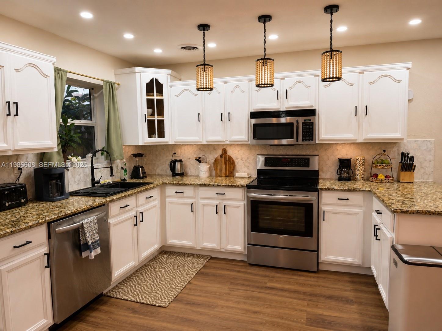 A kitchen features white cabinets, granite countertops, stainless steel appliances, and three hanging pendant lights — 1507 Harding St, Hollywood FL 33020, HOLLYWOOD, FL