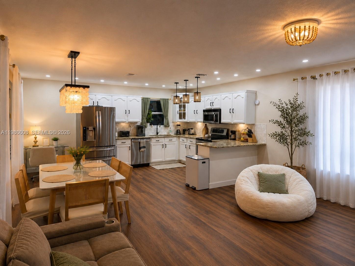 An open-concept kitchen and dining area features white cabinetry, stainless steel appliances, and wood flooring — 1507 Harding St, Hollywood FL 33020, HOLLYWOOD, FL