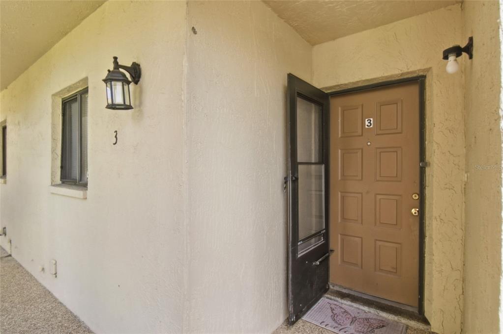 An exterior view of a tan building entrance with a brown door labeled number three — 7104 KIRSCH COURT UNIT 3, NEW PORT RICHEY, FL