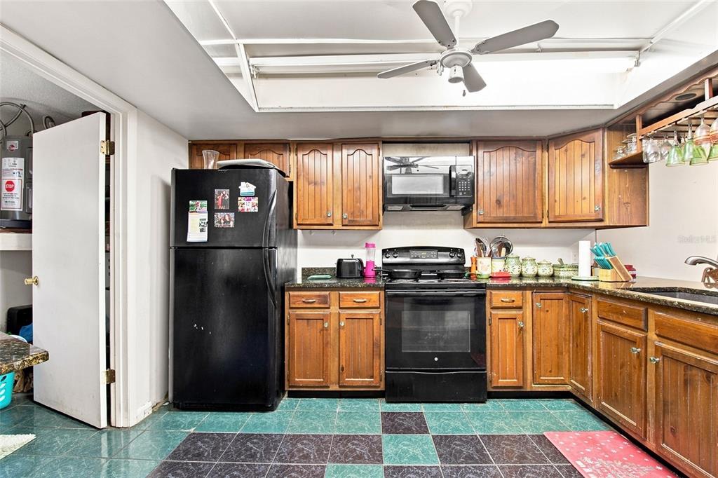 A kitchen features wood cabinets, black appliances, dark countertops, and a checkered green and black floor — 7104 KIRSCH COURT UNIT 3, NEW PORT RICHEY, FL