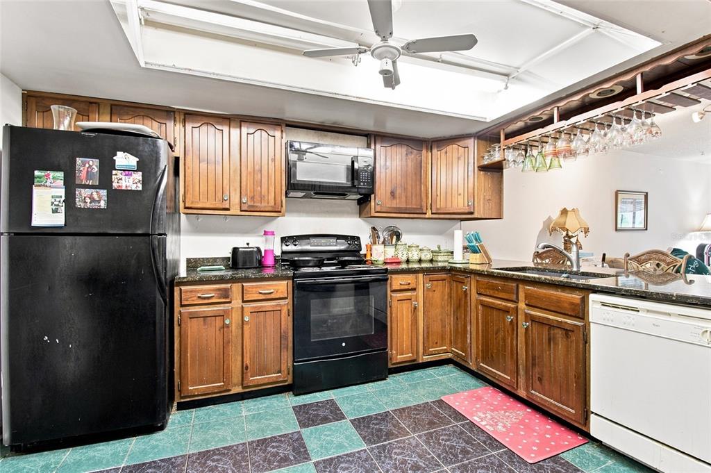 A kitchen features wooden cabinets, black appliances, a white dishwasher, and checkered floor tiles — 7104 KIRSCH COURT UNIT 3, NEW PORT RICHEY, FL