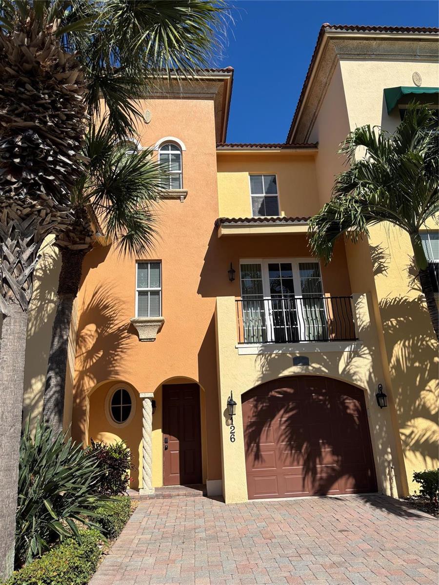 A three-story stucco townhouse with a garage, balcony, and paved driveway under a clear sky — 126 Ocean Bay Drive, Jensen Beach FL 34957, JENSEN BEACH, FL
