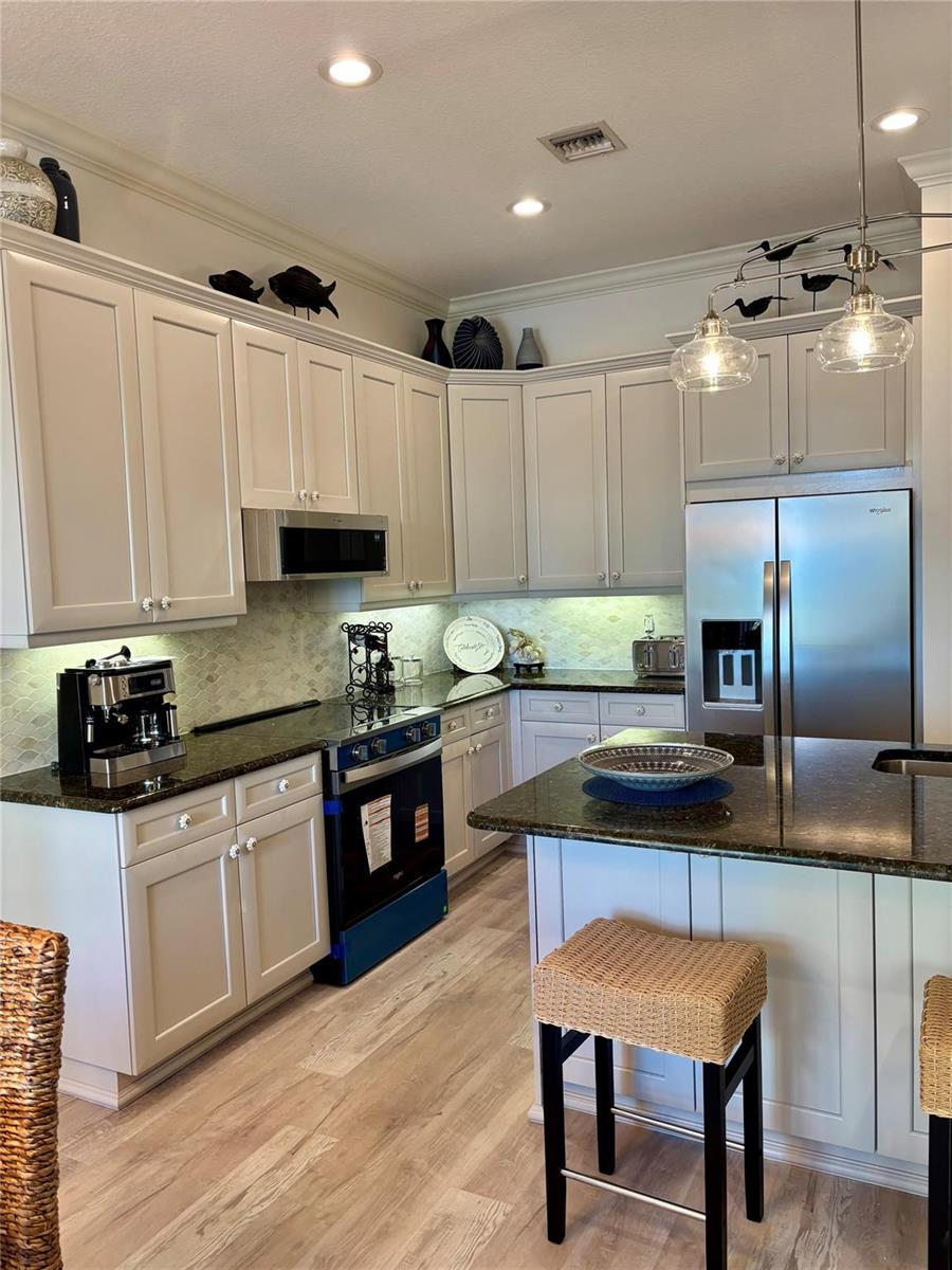 A kitchen features light-colored cabinets, dark granite countertops, stainless steel appliances, and a central island — 126 Ocean Bay Drive, Jensen Beach FL 34957, JENSEN BEACH, FL