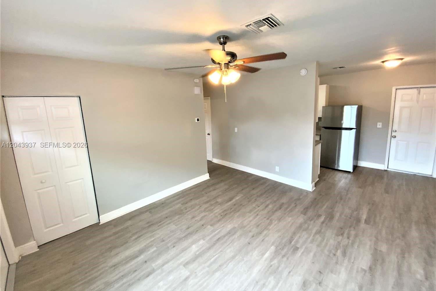 A living room features light gray walls, wood-look flooring, a ceiling fan, and a kitchen area — DELRAY BEACH, FL