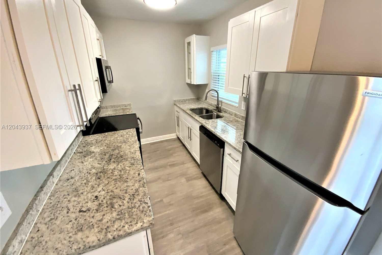 A galley kitchen features white cabinets, granite countertops, stainless steel appliances, and wood-look flooring — DELRAY BEACH, FL