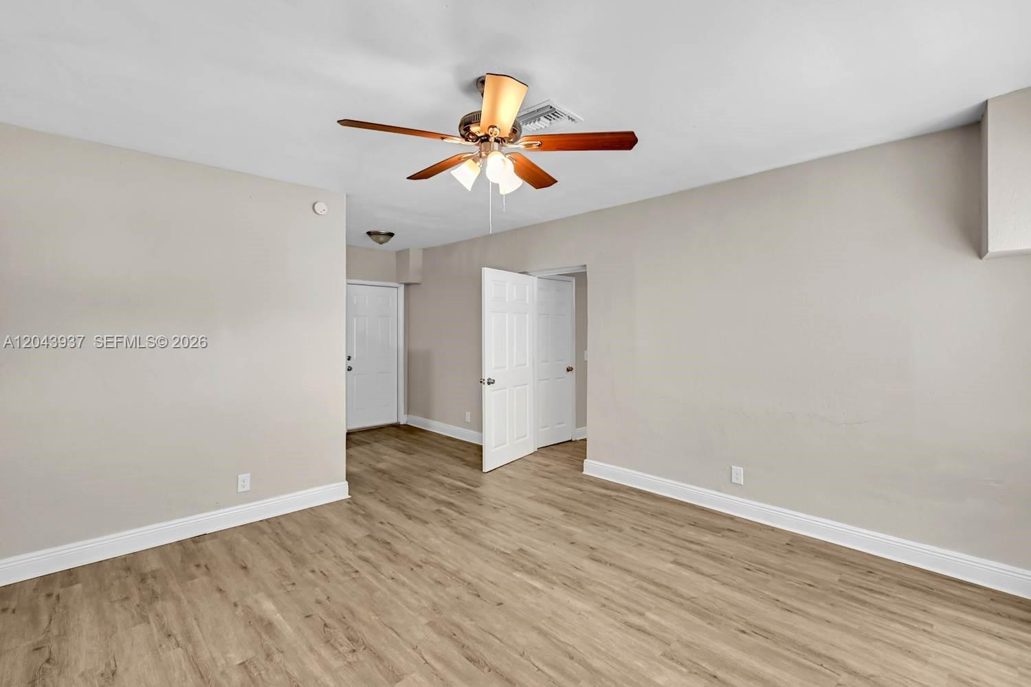 An empty room features light wood-look flooring, beige walls, and a ceiling fan — DELRAY BEACH, FL