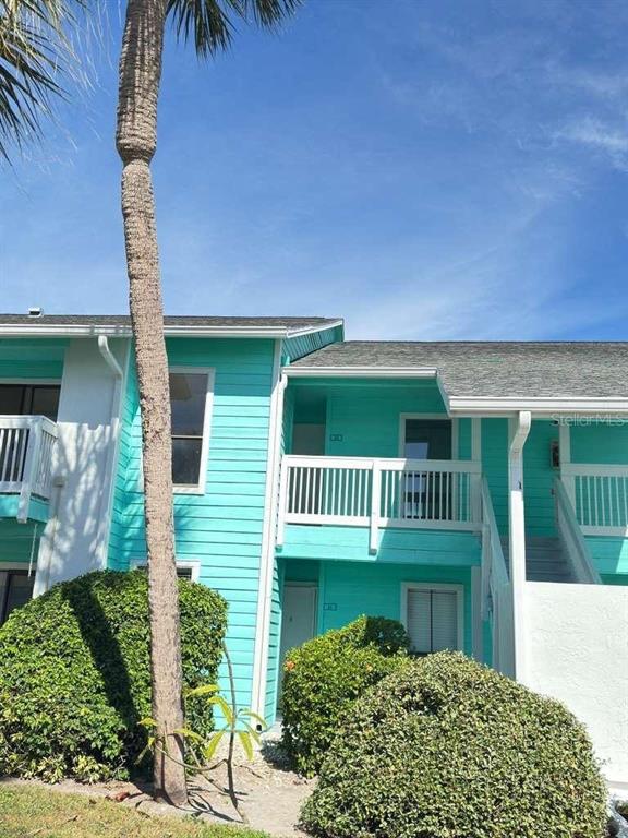 A two-story teal building features white railings, a palm tree, and manicured landscaping — 455 ALT 19 S UNIT 12, PALM HARBOR, FL