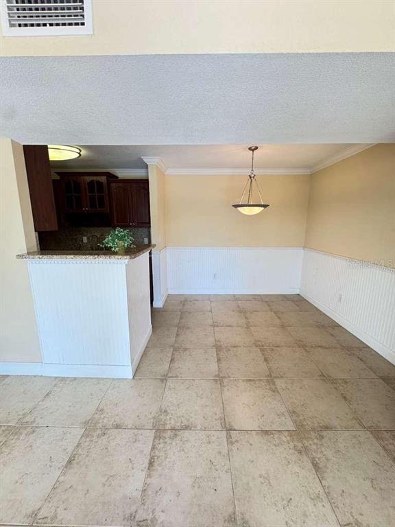 A dining area with tile flooring, white wainscoting, and a breakfast bar opening to a kitchen — 455 ALT 19 S UNIT 12, PALM HARBOR, FL